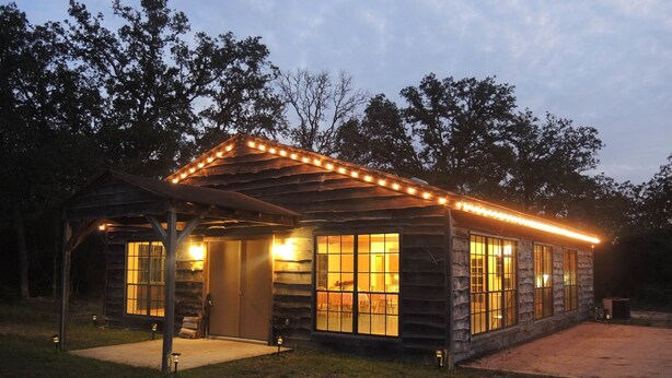 A rustic cabin with a covered porch and large windows, surrounded by trees.