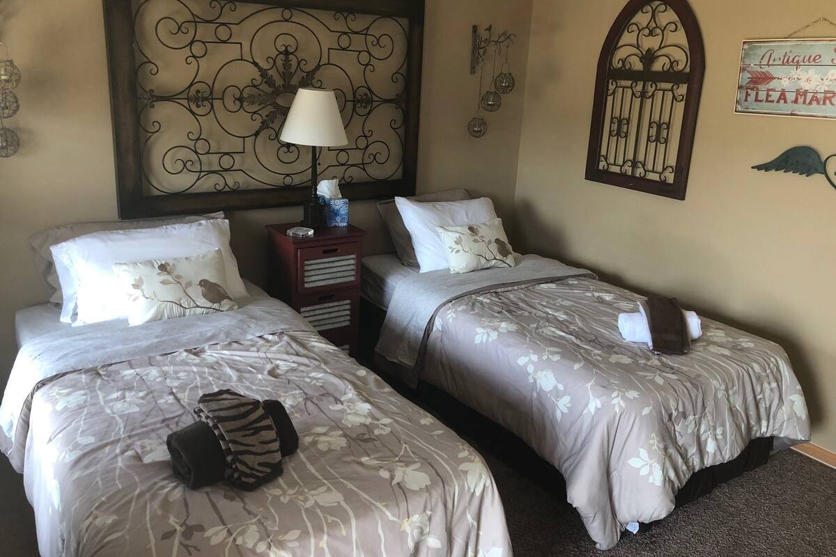 A hotel room with two single beds, a bedside table with a lamp, a decorative wall panel, and a sign.
