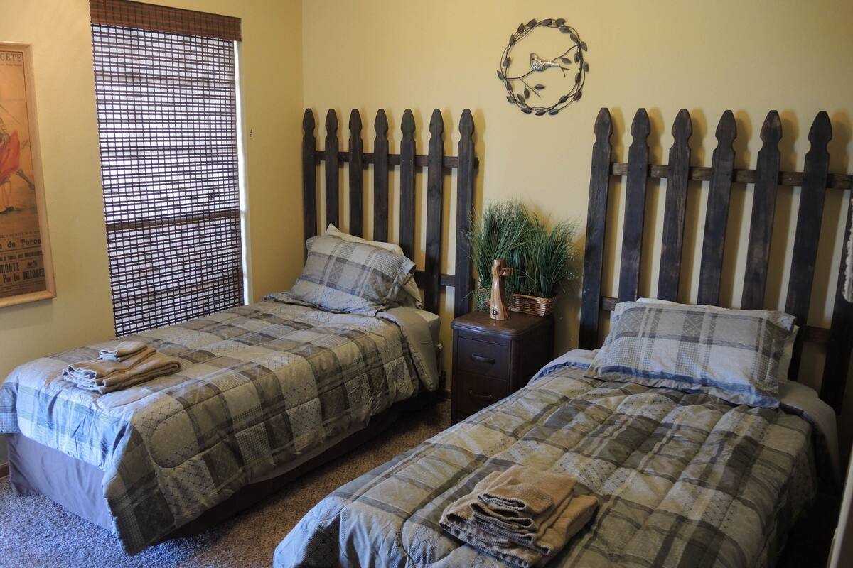 A bedroom with two beds, a wooden headboard, a wall decoration, and a window with blinds.