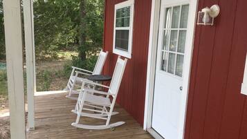 A wooden deck with two rocking chairs and a small table, adjacent to a red building with a white door and windows.
