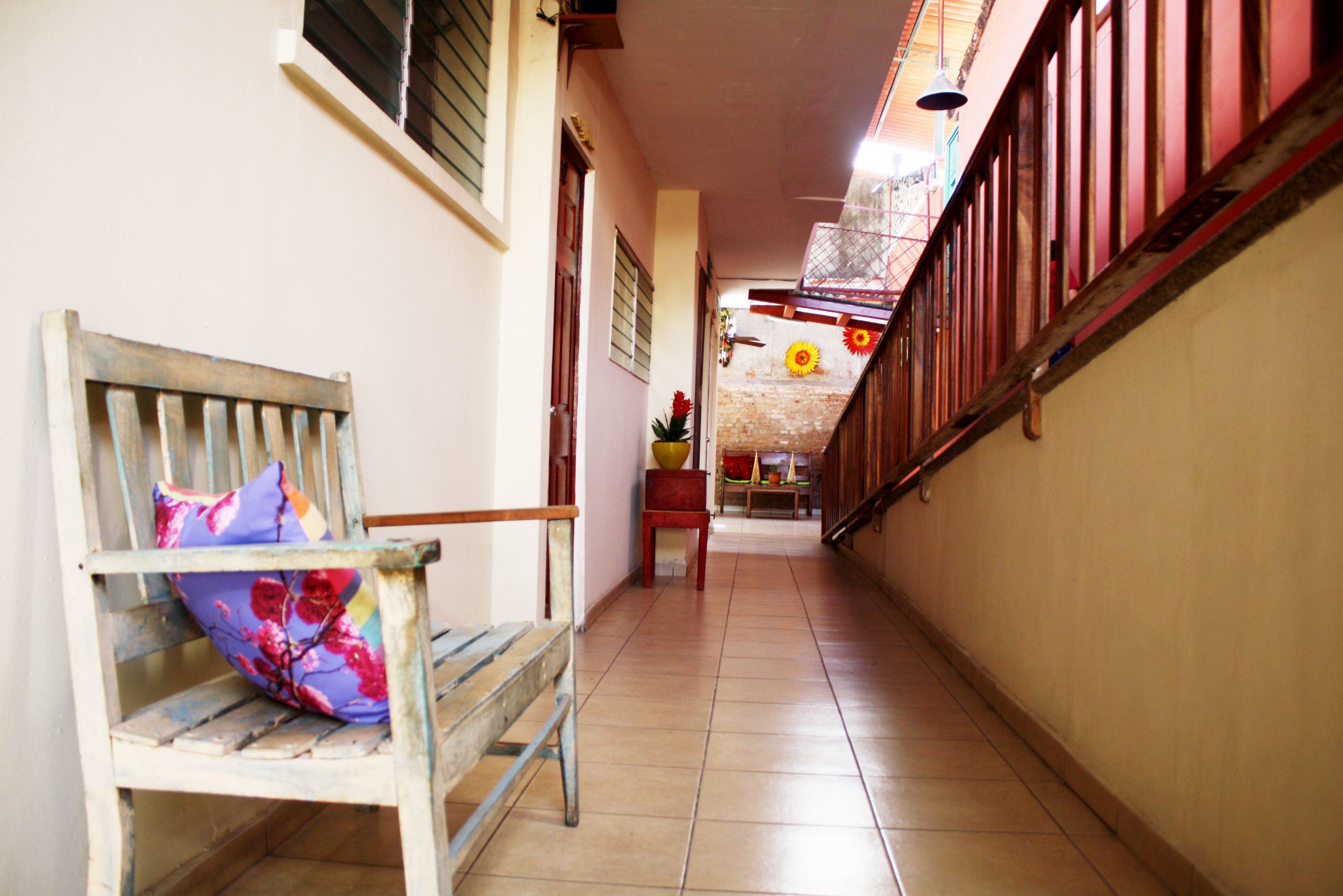 A narrow hallway with a wooden bench and a chair, a tiled floor, and a staircase with a red railing.