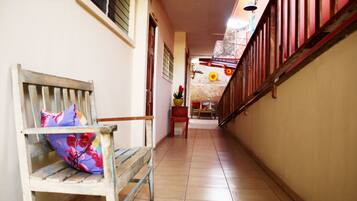 A narrow hallway with a wooden bench and a chair, a tiled floor, and a staircase with a red railing.