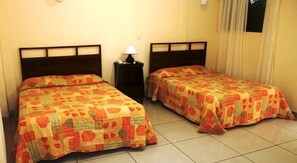 Dos camas individuales con cabeceras y pies de cama a juego, una mesita de noche con lámpara y una ventana con cortinas.