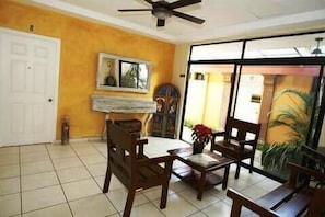 A room with a ceiling fan, a white door, a window with a view, and a tiled floor.
