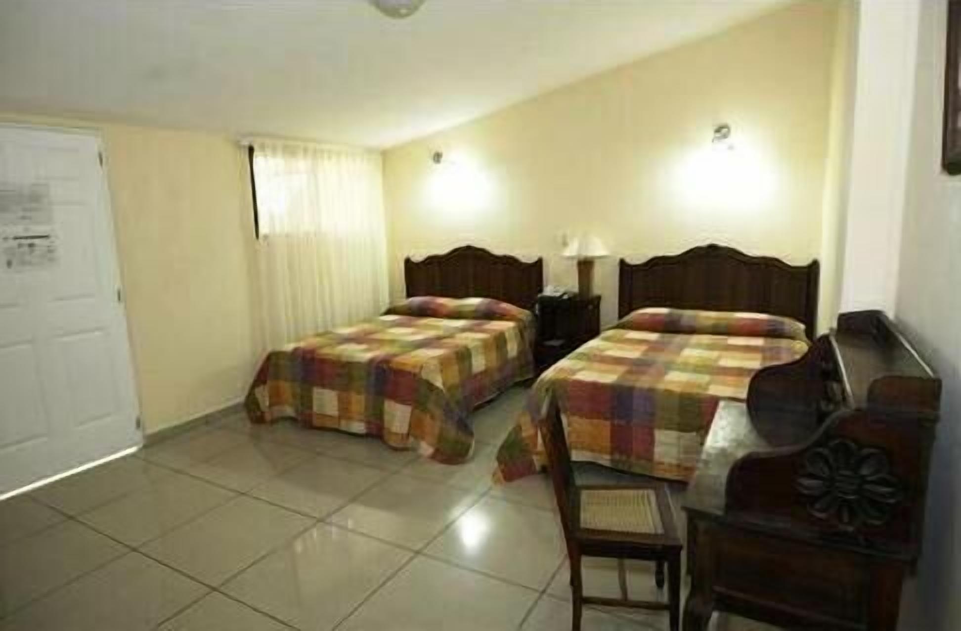 A room with two beds, a chair, a desk, and a door.