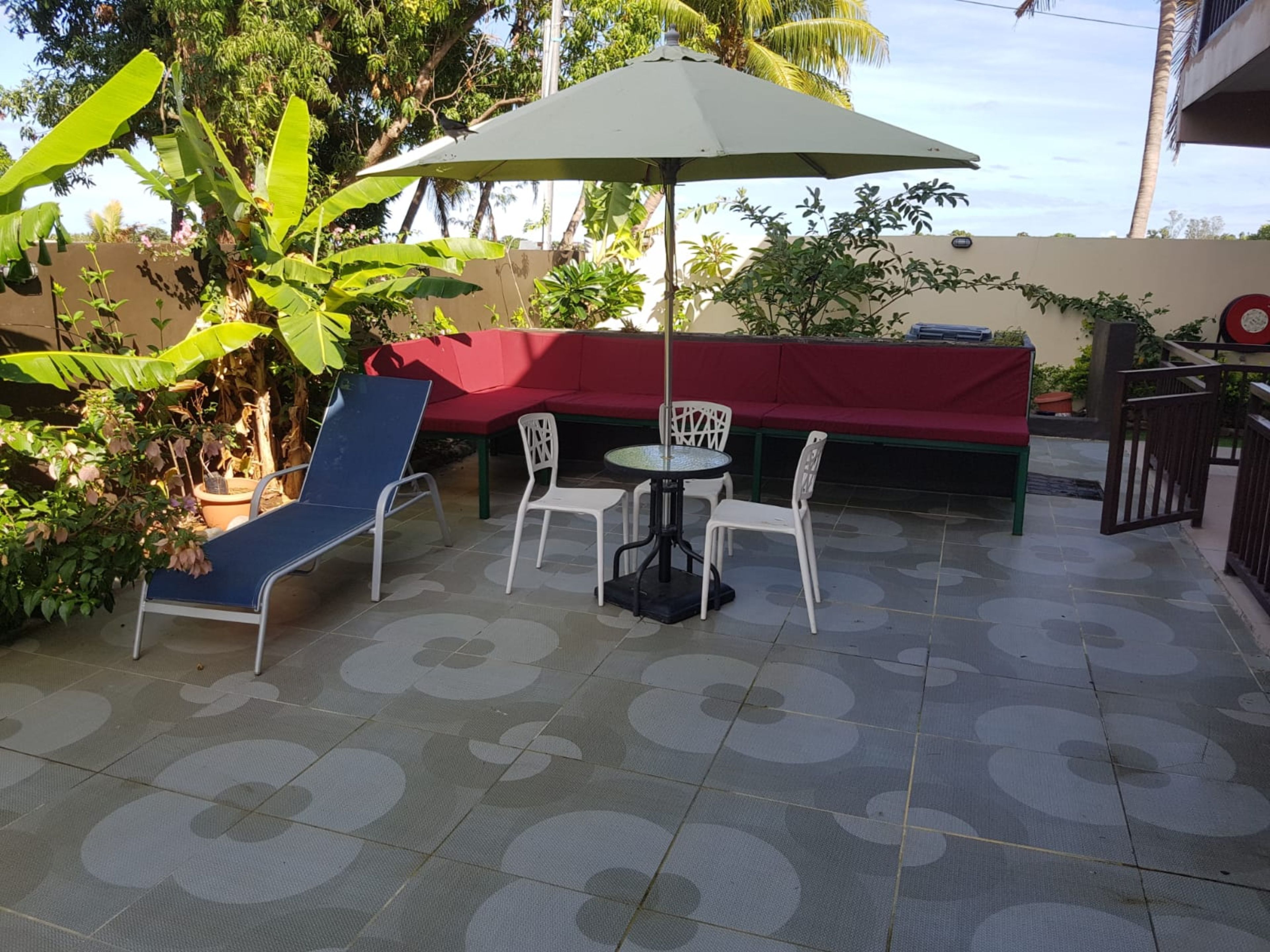 Um pátio com sofá vermelho, cadeiras brancas, mesa e um grande guarda-sol.