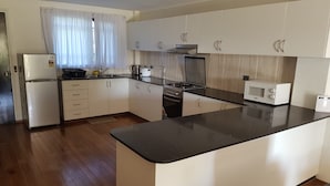 Une cuisine moderne avec des meubles blancs, un plan de travail noir, un réfrigérateur, une cuisinière et un four à micro-ondes.