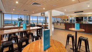 Un área de bar amplia con vista al océano, mesas y sillas de madera y un panel con la carta de The Beach Club.
