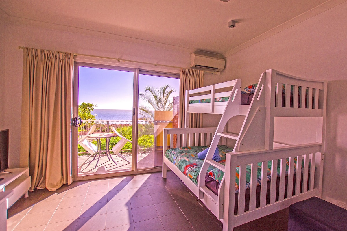 Quarto com beliche, televisão e varanda vista para o mar.
