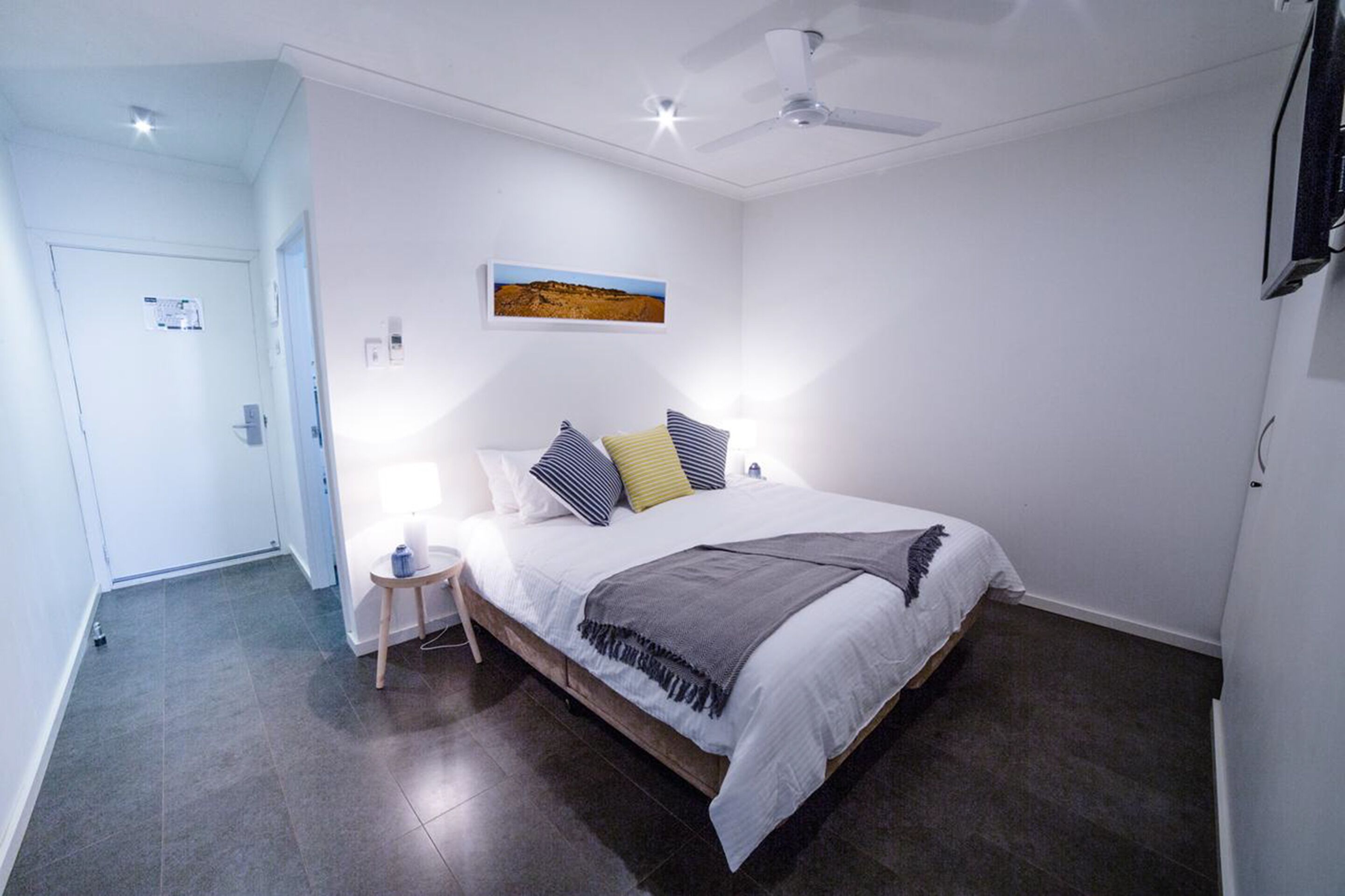 A bedroom with a bed, a bedside table, a ceiling fan, and a wall-mounted TV.