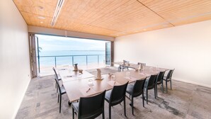 Un salón de conferencias con una gran mesa y sillas, vistas al mar a través de un ventanal y un techo de madera.