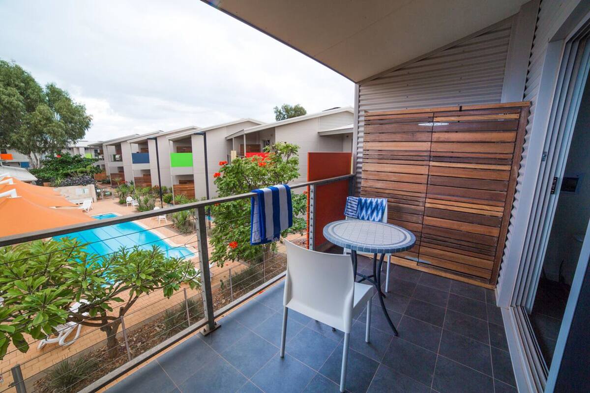 Uma varanda com piscina, cadeiras brancas e uma mesa.