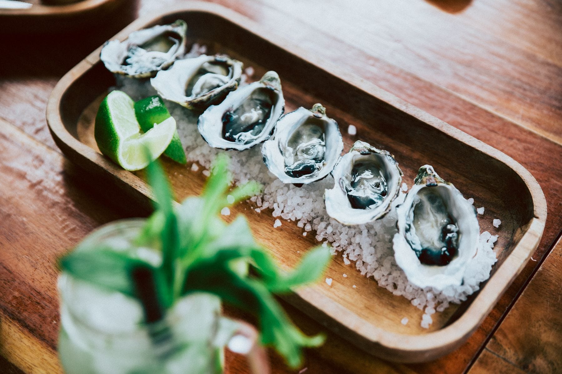 A wooden tray with oysters, lime, and salt on a wooden table.