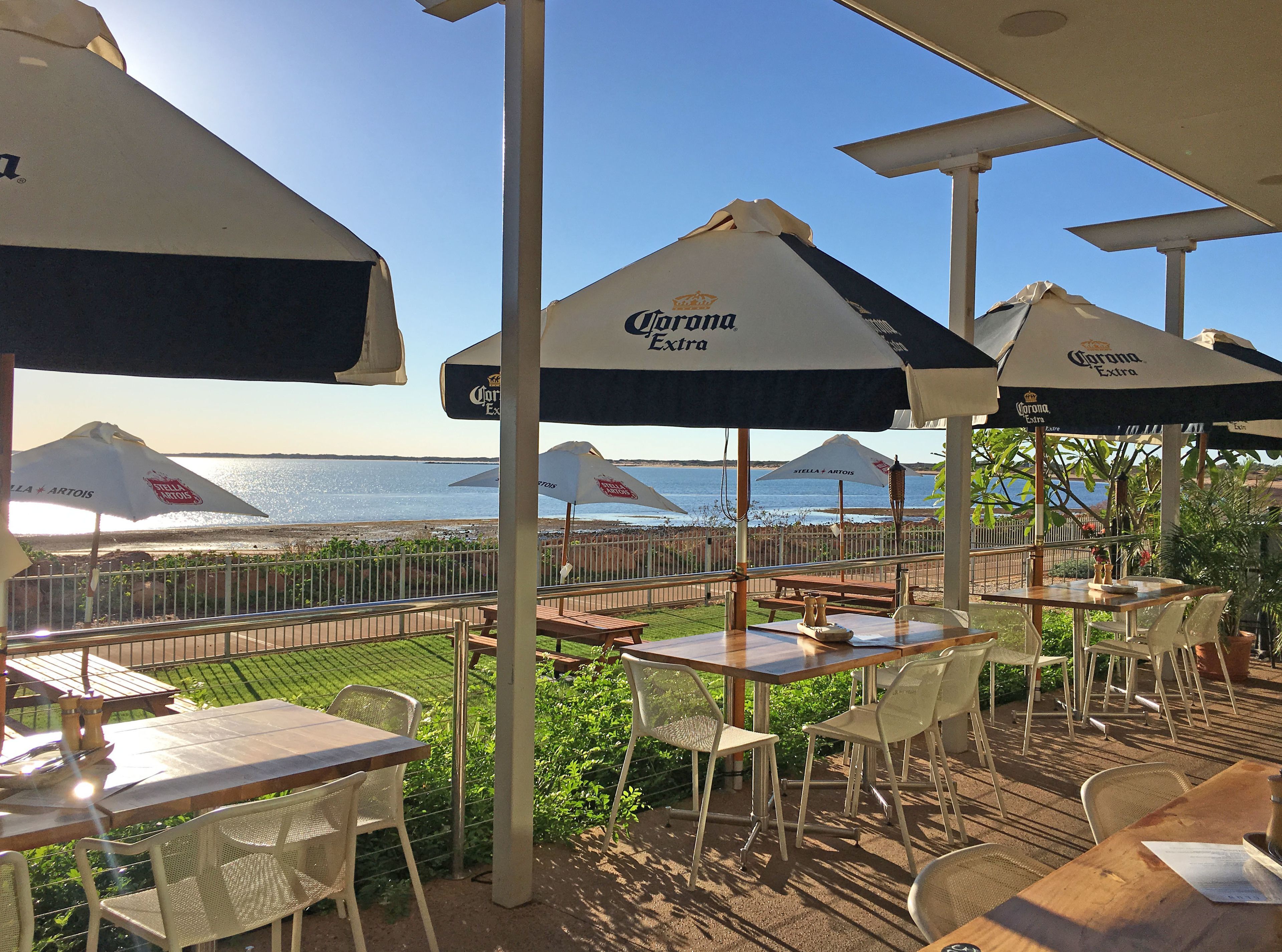 An outdoor seating area with tables and chairs under umbrellas, overlooking a beach.