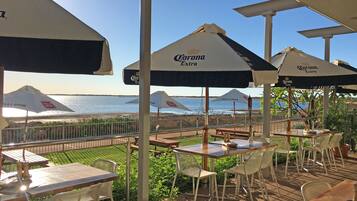 An outdoor seating area with tables and chairs under umbrellas, overlooking a beach.