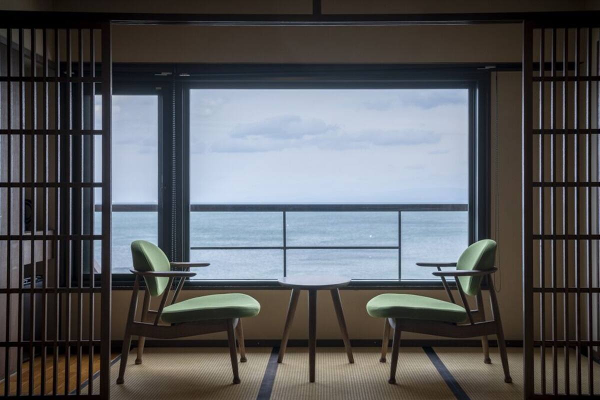 A room with a view of the sea, two chairs, a small table, and a traditional Japanese sliding door.