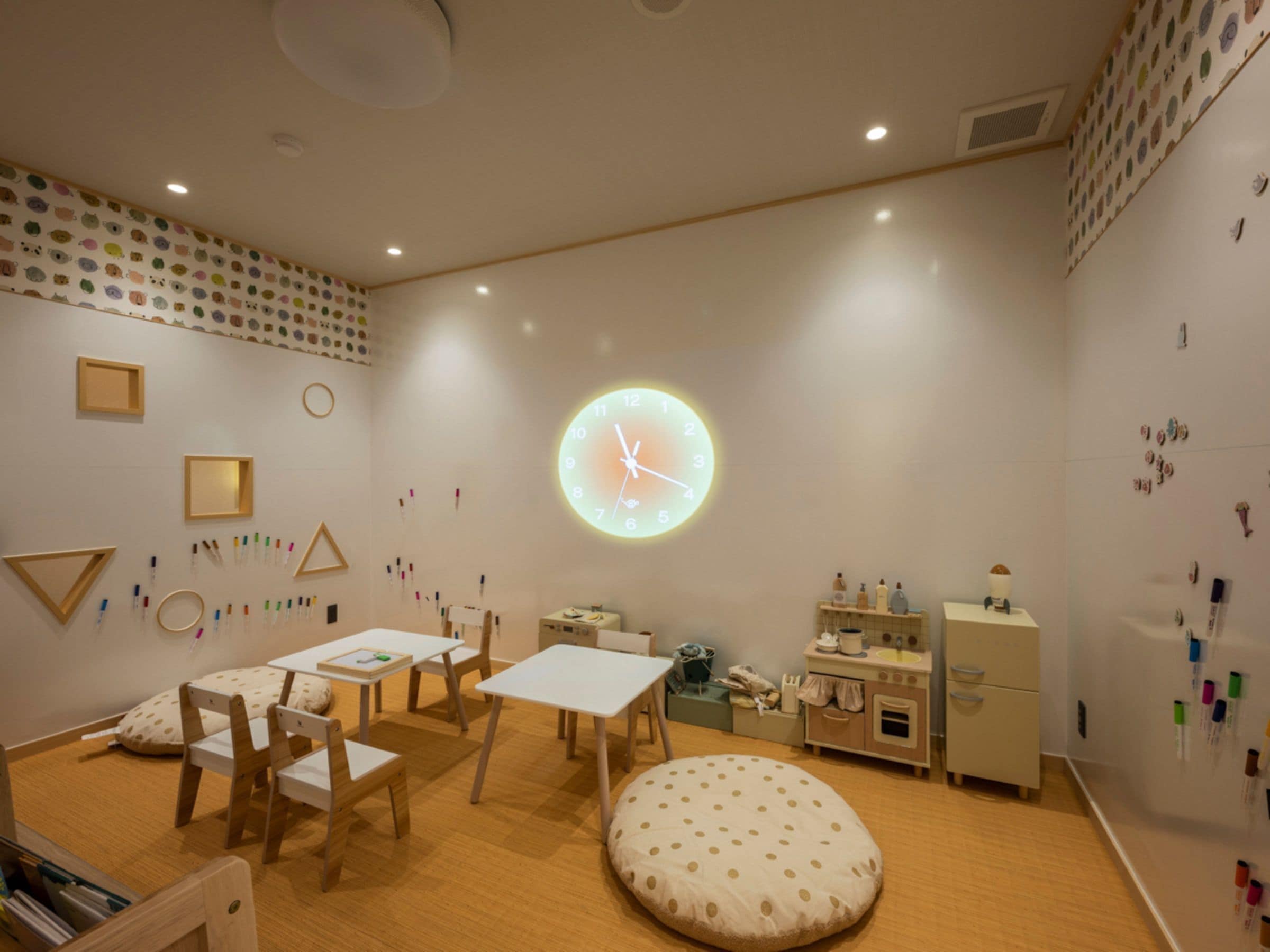 A children's playroom with a round wall clock, wooden furniture, and educational wall decorations.