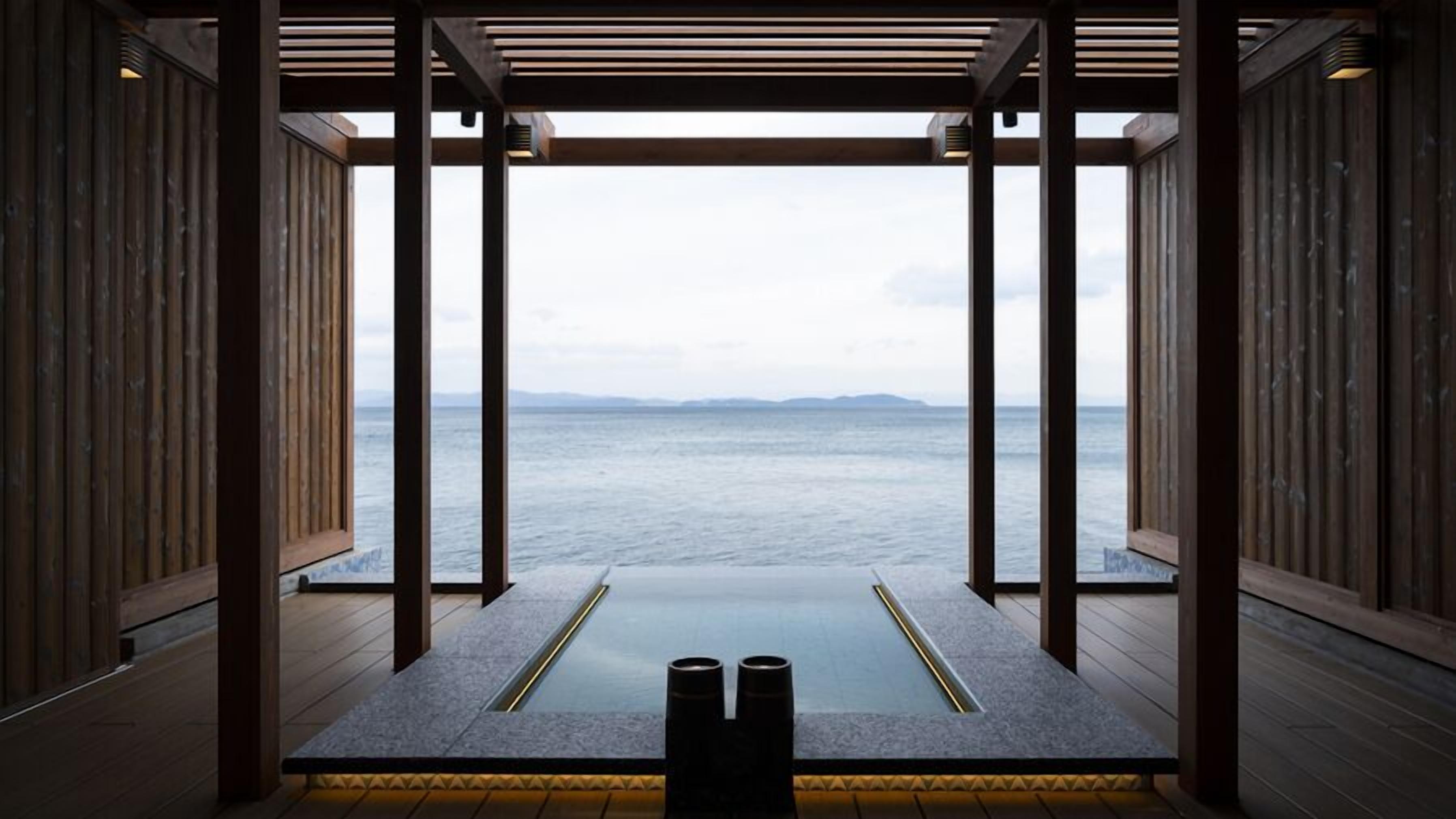 A room with a view of the sea, wooden walls, and a stone floor.