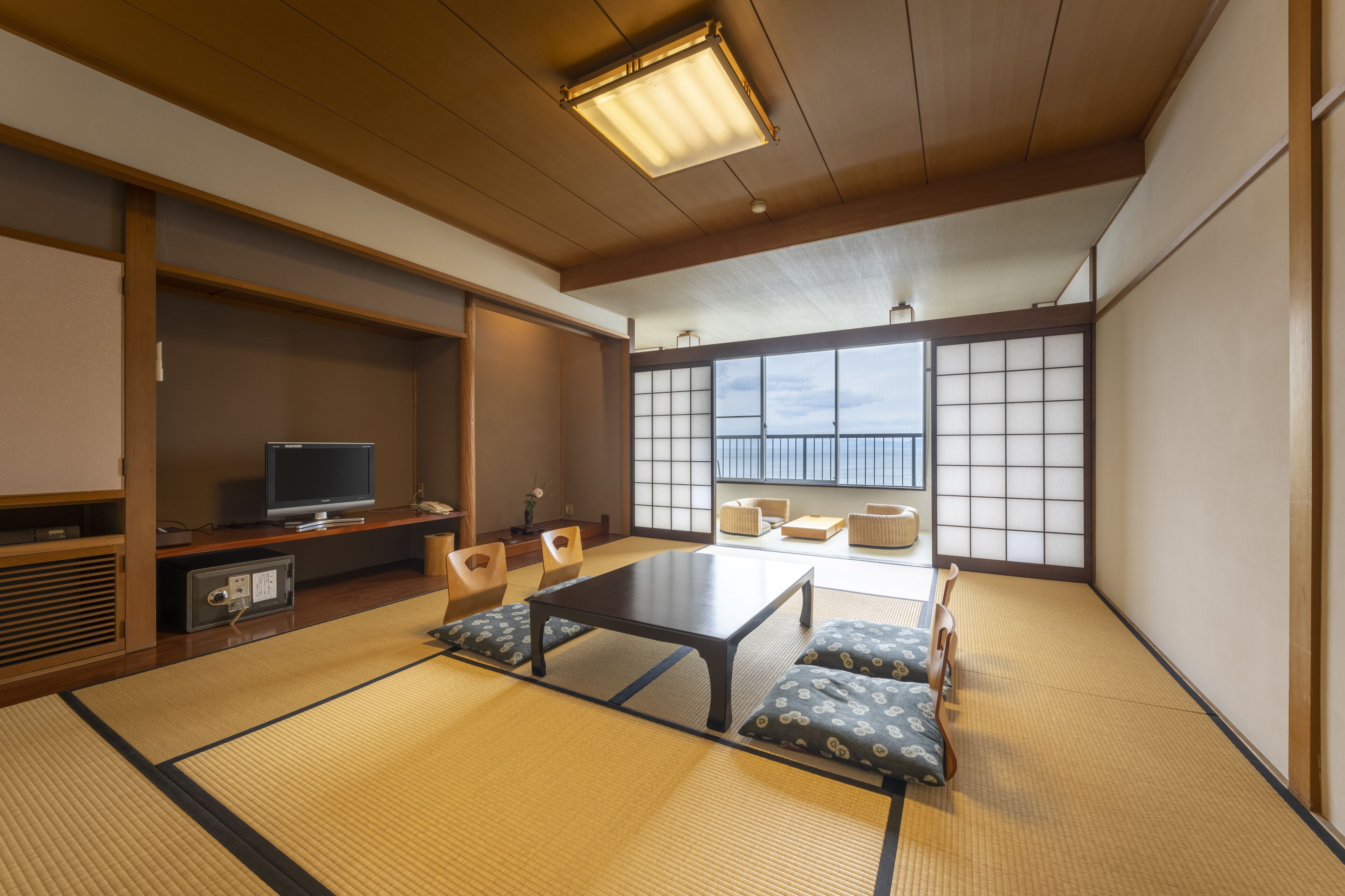 Una habitación japonesa tradicional con suelo de tatami, una mesa baja, cojines, televisión y puertas correderas.