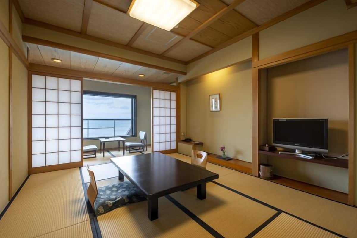 Ein traditioneller japanischer Raum mit Tatami-Böden, einem niedrigen Tisch, einem Fernseher und Blick aufs Meer.