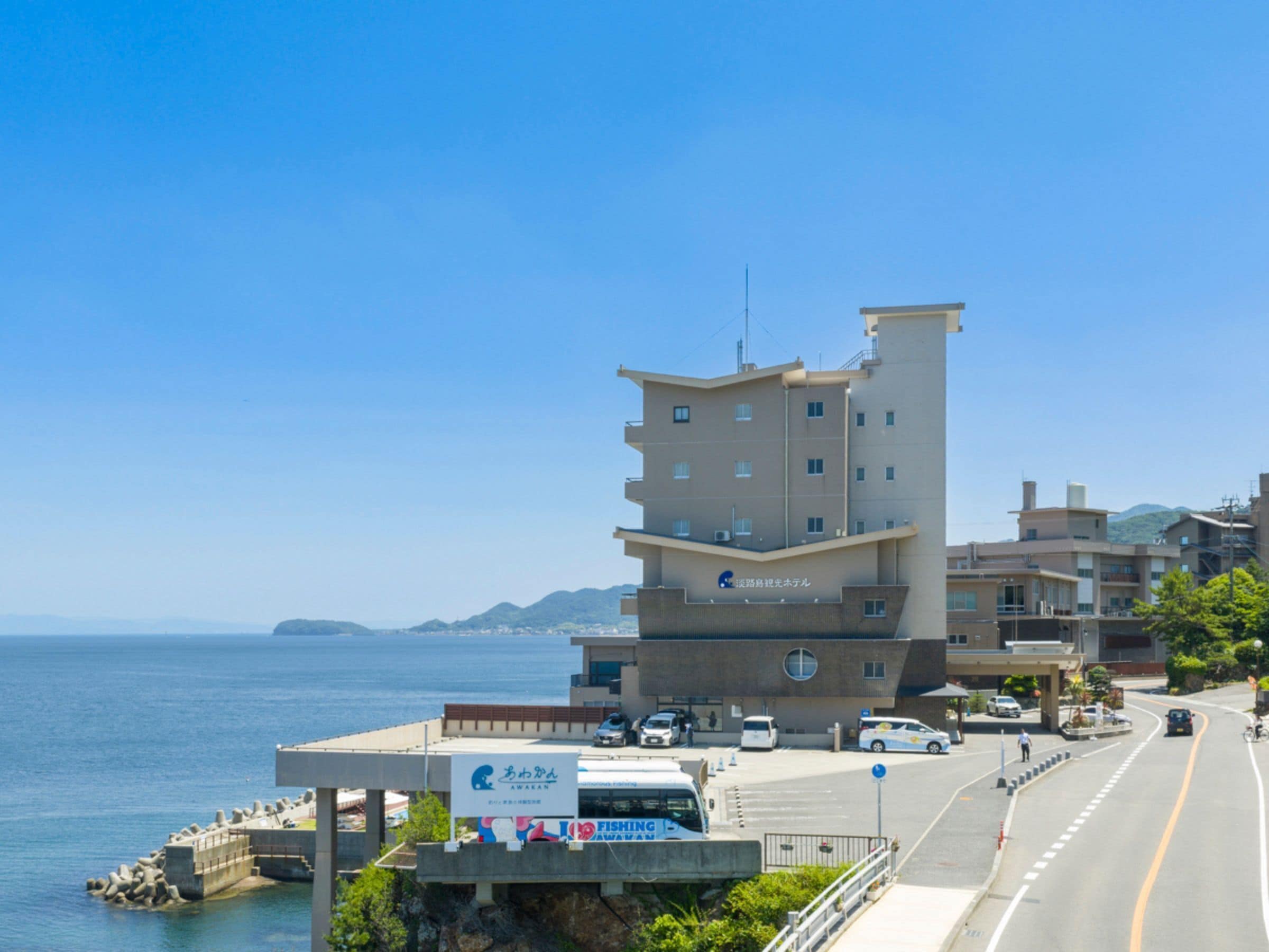 A coastal building with multiple floors, a signboard, and a road with vehicles and a pedestrian.