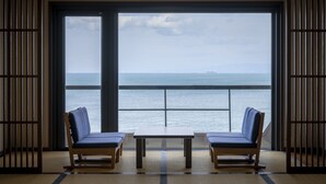 A room with a large window overlooking the sea, two blue chairs, and a small table. - Awakan (Sumoto)