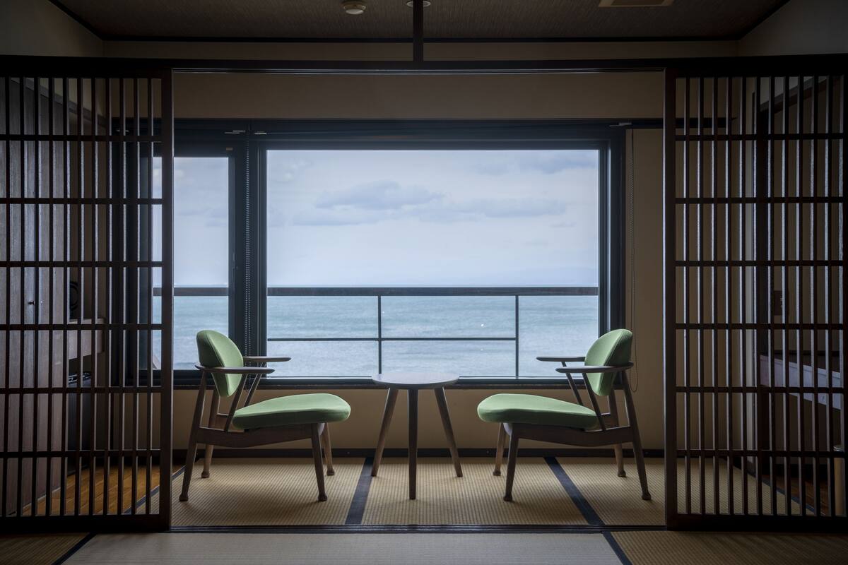 A room with tatami mats, a low table, and two green chairs.