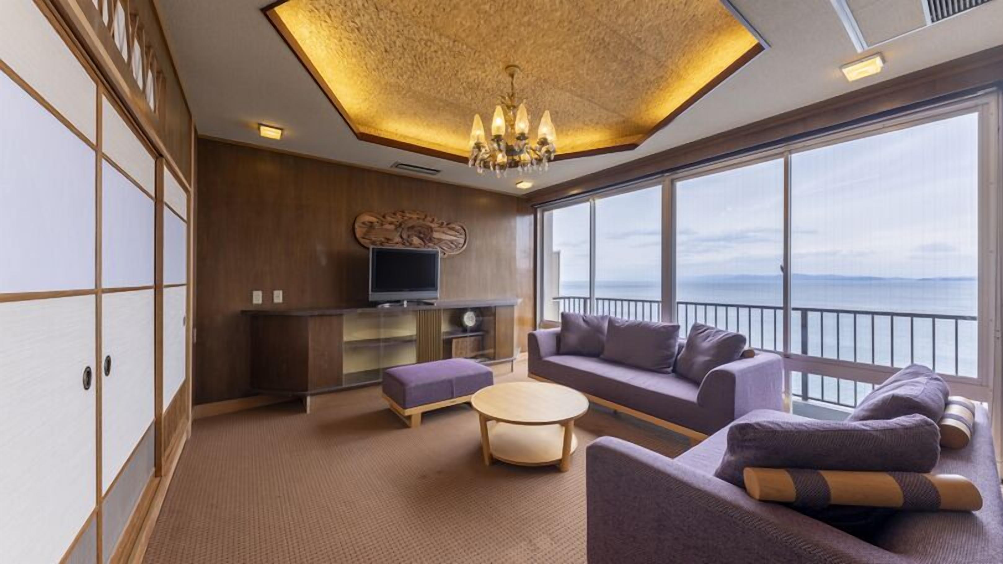 A modern living room with a sofa set, a television, and a view of the sea.