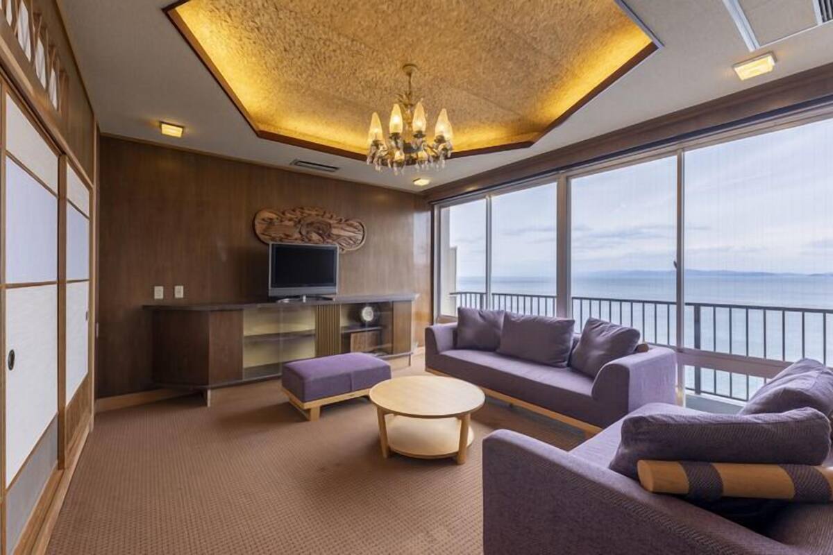 A modern living room with a sofa set, a television, and a view of the sea.