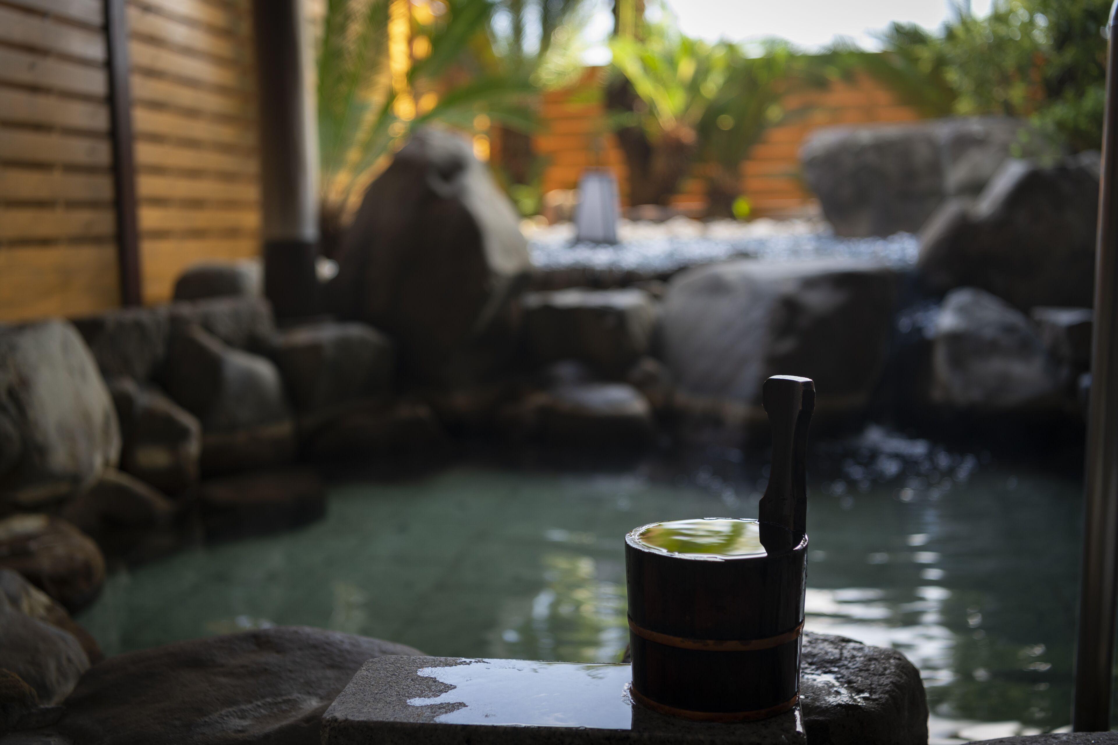 A stone bench with a cup and straw by a water feature with rocks and greenery.