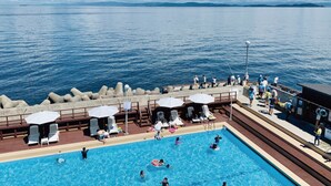 A pool area with a view of the sea, lounge chairs, umbrellas, and a lifeguard on duty. - Awakan (Sumoto)