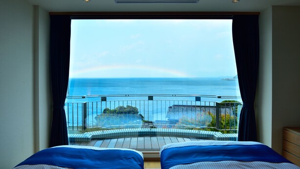 Un dormitorio con un amplio ventanal que da a un balcón con vistas al mar y un arcoíris.