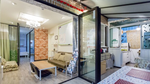 A modern hotel room with a glass partition, a sofa, a small table, and a kitchen area visible through the partition. - Xicun 168 B&B (Seoul)