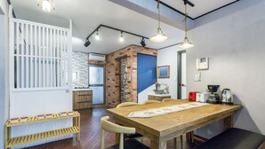 A dining area with a wooden table, chairs, and a bench. There is a kitchen area in the background with a brick wall and a blue door. - Xicun 168 B&B (Seoul)