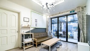 A modern room with a sofa, a small table, a white cabinet, and a large window with a view of the outside. - Xicun 168 B&B (Seoul)