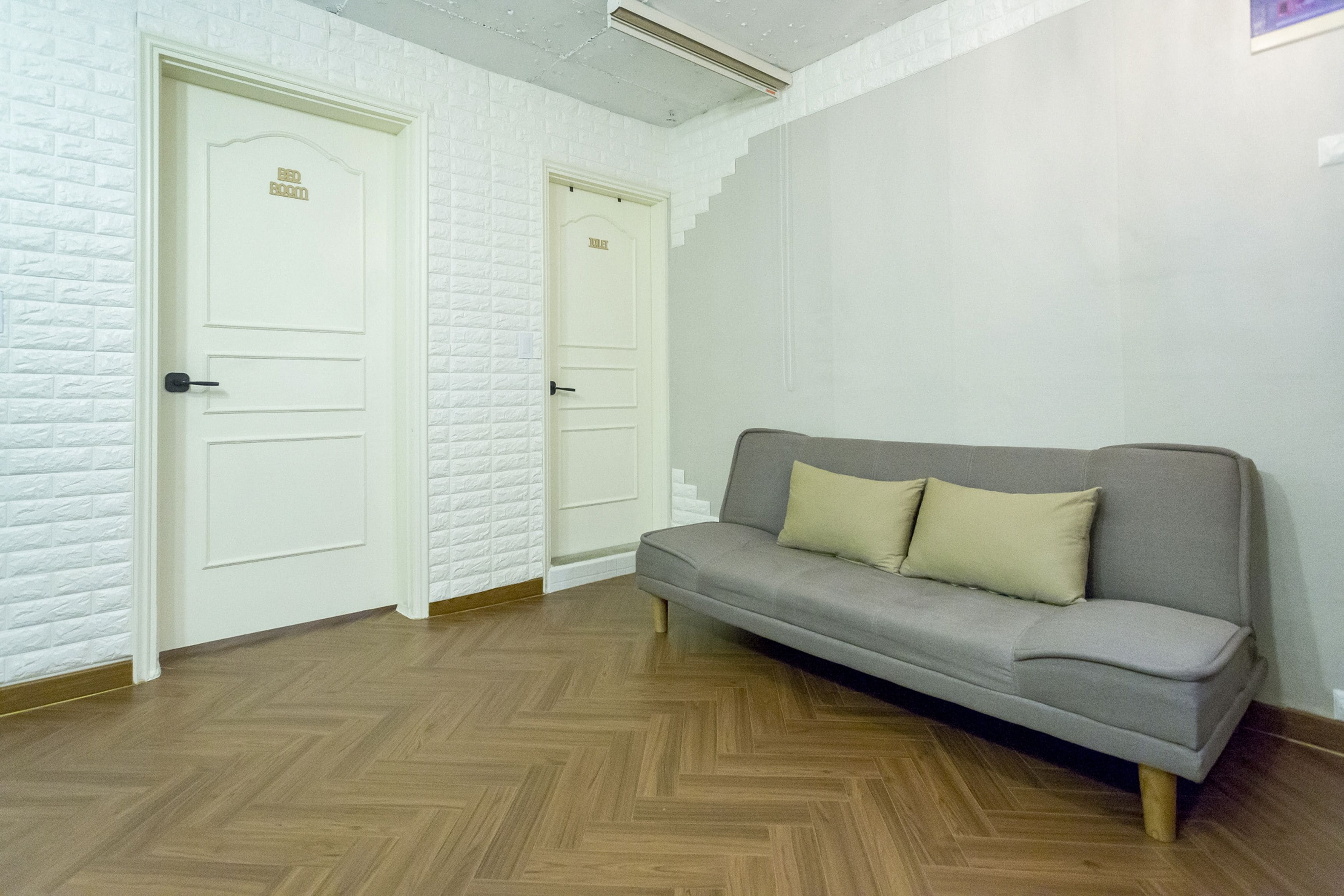 Una habitación con un sofá gris, paredes con diseño de ladrillo blanco y suelo de madera.