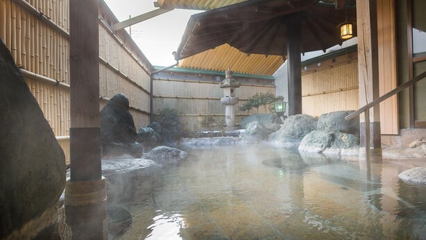 Ein traditionelles japanisches Onsen mit Steinbädern, Holzarchitektur und gefliestem Boden.