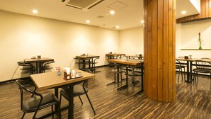 Ein Restaurantinneres mit mehreren Tischen und Stühlen, Holzelementen und Deckenleuchten.