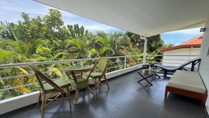 A balcony with a table and chairs, a lounge chair, and a view of lush greenery.