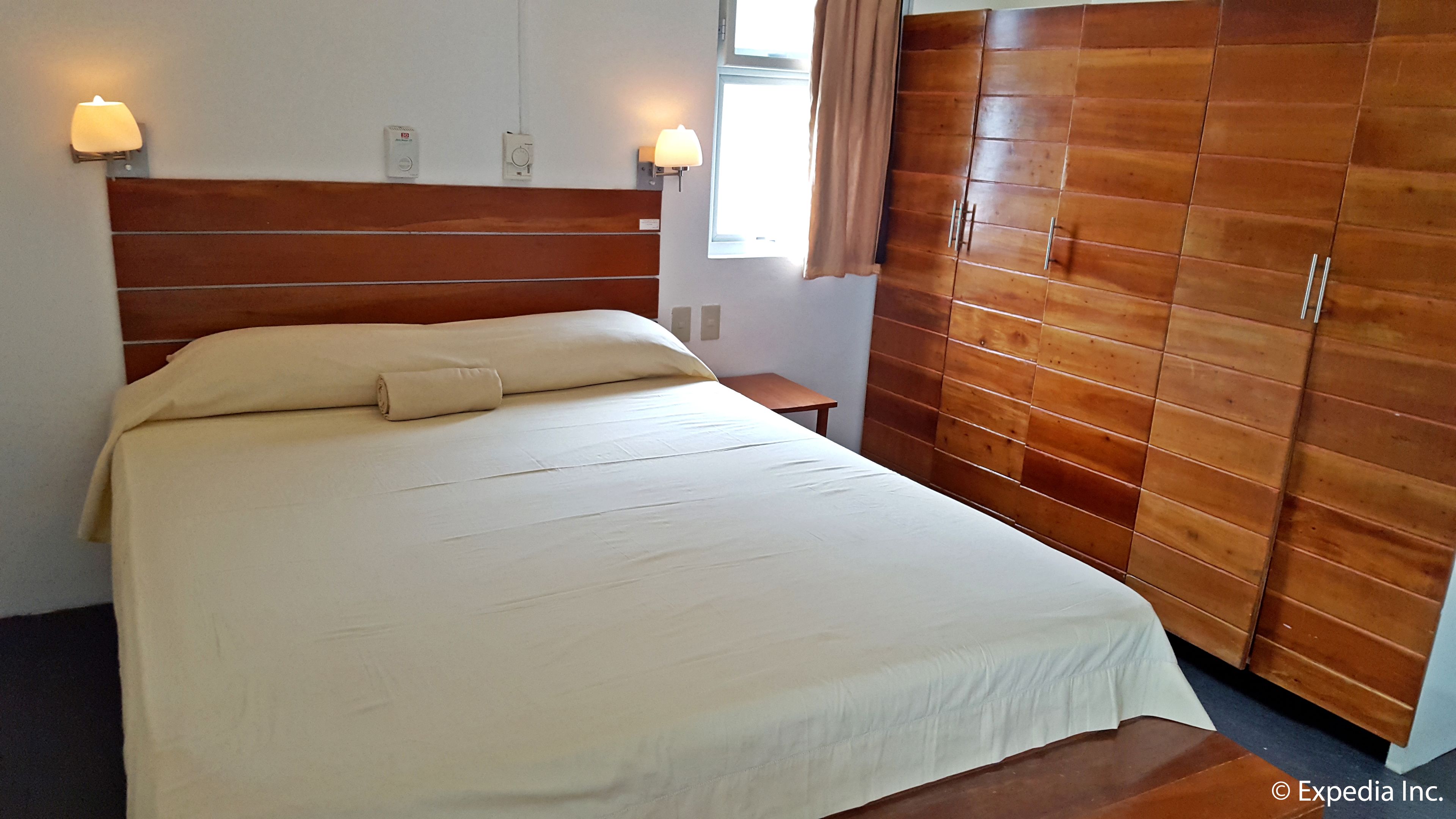 A hotel room with a large bed, a wooden wardrobe, and two wall-mounted lamps.