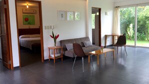 A modern living room with a sofa, chairs, a coffee table, and a bed in the background.