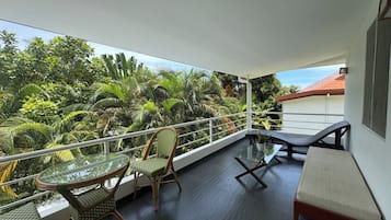 Ein Balkon mit Glastisch und Stühlen, einer Sitzecke und Blick auf üppiges Grün.