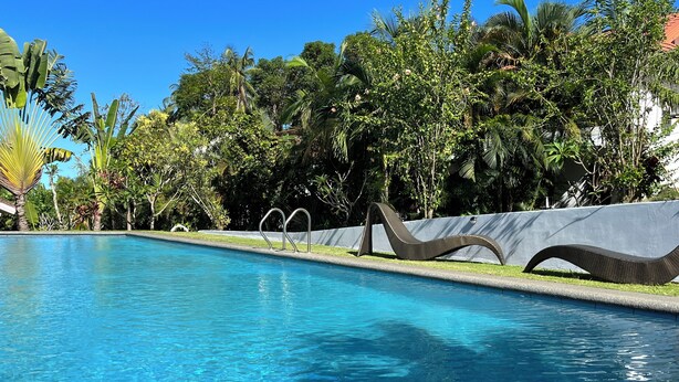 A swimming pool with clear blue water, surrounded by lush greenery and a decorative metal sculpture.