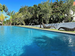 A swimming pool with clear blue water, surrounded by lush greenery and a decorative metal sculpture. - MarPas Apartments (Valencia)