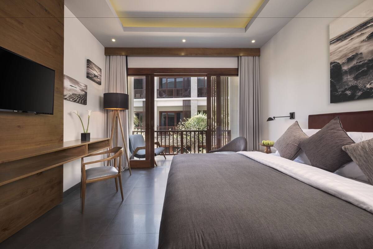 Une chambre d’hôtel moderne dotée d’un grand lit, d’un bureau, d’une télévision et d’un balcon offrant une vue sur l’immeuble.