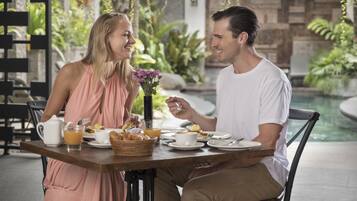 Una pareja cenando en una mesa con vista a una piscina y follaje.