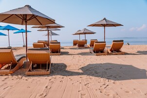 Una playa con hileras de sillones de mimbre y sombrillas, dispuestas para tomar el sol.