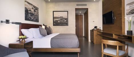 A modern hotel room with a large bed, a desk, a chair, a TV mounted on the wall, and artwork on the walls.