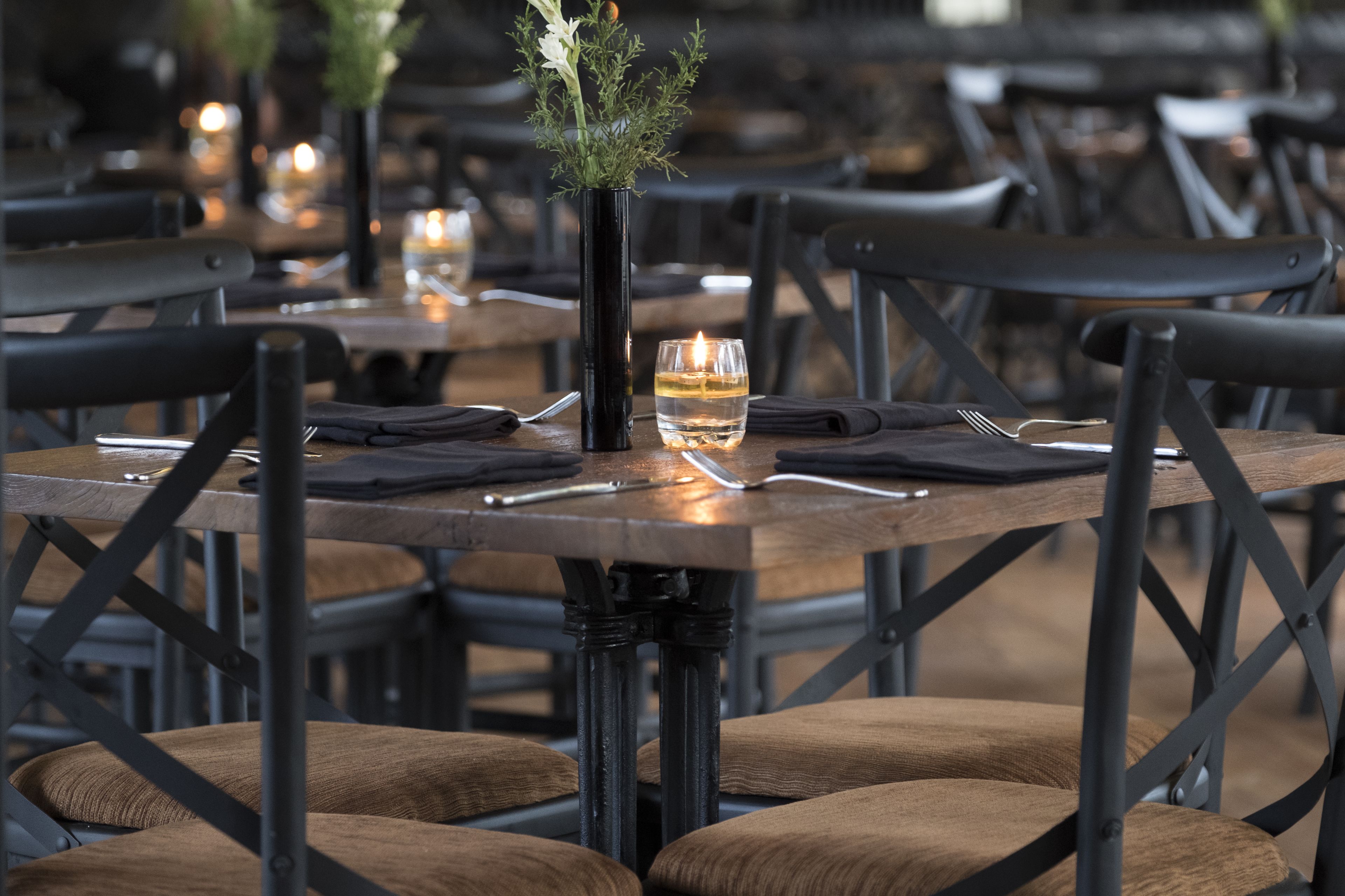 Un salón de restaurante con mesas de madera, sillas de metal negro y velas.