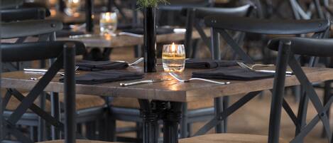 Un salón de restaurante con mesas de madera, sillas de metal negro y velas.